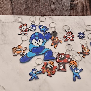 Könnte beinhalten: Eine Sammlung von Pixel-Art-Schlüsselanhängern mit Mega-Man-Charakteren in verschiedenen Posen und Farben, darunter Blau, Rot, Orange und Weiß. Jeder Schlüsselanhänger ist aus kleinen Kunststoffperlen gefertigt und an einem silbernen Metallring befestigt.