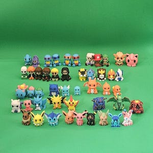 May include: A collection of small, colorful plastic character figurines arranged in rows. The set includes various creatures with distinct shapes, facial features, and color palettes, including shades of blue, yellow, pink, orange, and green.