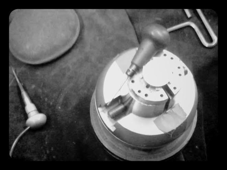 May include: A black and white image of a metal jewelry making tool with a small metal rod attached to a handle. The tool is used to hold jewelry pieces in place while they are being worked on.