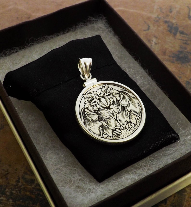 May include: A silver pendant featuring a detailed engraved design of two owls facing each other. The pendant is round and has a bail for attaching a chain.