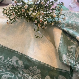 May include: Two white and green tablecloths with a floral pattern. The tablecloth is made of a soft, woven fabric. A bouquet of white flowers is on top of the tablecloths.