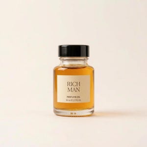Könnte beinhalten: Eine klare Glasflasche mit bernsteinfarbenem Parfümöl, einem schwarzen Schraubverschluss und einem rechteckigen cremefarbenen Etikett. Auf dem Etikett steht der Text RICH MAN, PERFUME OIL, 50 ml und 1.7 FL. OZ. in dunkelbrauner Schrift.