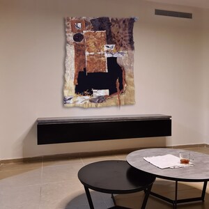 May include: Abstract art piece with brown, black, and white colors. The art is framed and hanging on a wall above a black shelf. The shelf is mounted on a wall in a room with a light brown tiled floor.
