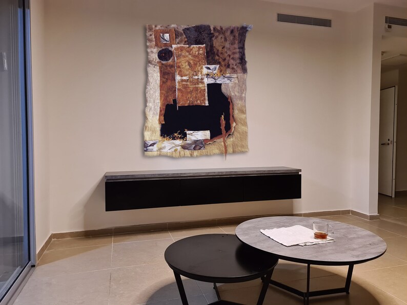 May include: Abstract art piece with brown, black, and white colors. The art is framed and hanging on a wall above a black shelf. The shelf is mounted on a wall in a room with a light brown tiled floor.