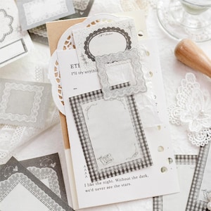 Puede incluir: Una colección de papelería decorativa con marcos de encaje blanco, una pegatina rectangular con borde de cuadros vichy en blanco y negro, y una tarjeta blanca impresa con el texto I like the night. Without the dark, we'd never see the stars.