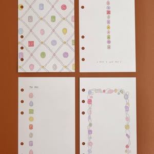May include: Four white planner refill pages with six-hole punches. One page features a diamond-shaped chain pattern with colorful gemstones. Another has a vertical list of gems and the text 'DATE/' and 'What a good day!'. A third has 'TO DO:' with gem bullets. The last has a gem-encrusted border.