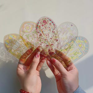 May include: A set of five arched, transparent plastic bookmarks featuring intricate stained-glass style patterns with floral motifs in shades of pink, yellow, blue, and green. Each bookmark has a rounded top and a small hole punched at the base.