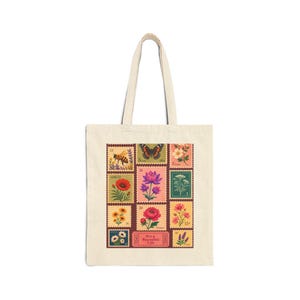 May include: A cream-colored canvas tote bag featuring a rectangular graphic print of various vintage-style postage stamps. The stamps display illustrations of flowers, a butterfly, and a bee, with a central ticket reading It's a Beautiful Life.