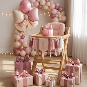 May include: A wooden high chair decorated with a pink number one banner, tassels, and bows. A small pink cake sits on the tray. A large balloon arch in shades of pink and cream surrounds the chair, and several gift boxes wrapped in pink paper with large bows are arranged on the floor.