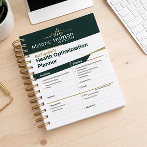 Op de afbeelding: Een spiraalgebonden planner met een donkergroene en witte kaft met de tekst "Metiric Human" en "Biohacker's Health Optimization Planner". De binnenpagina toont secties voor tracking, statistieken en bloedonderzoek met een gouden spiraal.