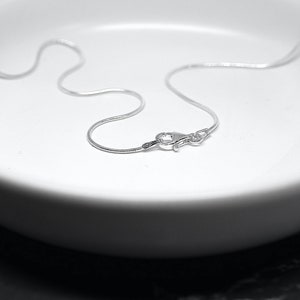 May include: A silver chain necklace with a lobster clasp fastening. The chain is on a white surface.