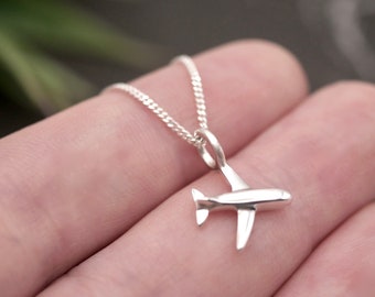 Könnte beinhalten: Eine Halskette mit einem silbernen Flugzeug-Anhänger. Der Anhänger ist ein schlichtes, minimalistisches Design eines Flugzeugs im Flug.