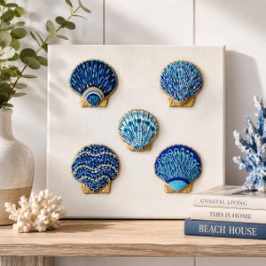 Op de afbeelding: Een vierkant wit canvas met vijf decoratieve schelpen in een vijfhoekig patroon. Elke schelp is beschilderd in blauw- en wittinten met gouden randen. De schelpen vertonen verschillende patronen, waaronder strepen, stippen en golvende lijnen.