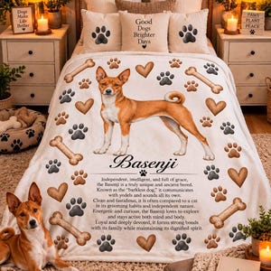 May include: A cream-colored fleece blanket featuring a central illustration of a brown and white Basenji dog, surrounded by brown heart and paw print patterns, bone graphics, and text detailing the breed's history and characteristics.