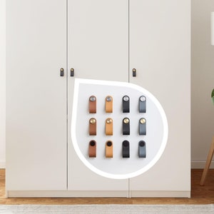 Pode incluir: Um conjunto de 12 puxadores de armário de couro com detalhes em latão. Os puxadores estão dispostos em forma de grade e estão disponíveis em três cores: marrom, bege e cinza.
