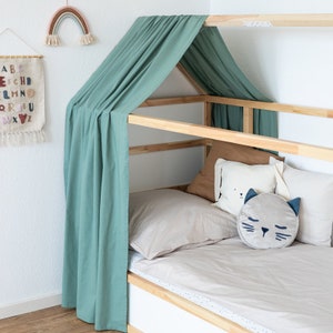 Ein Ikea Kura Kinderbett mit Dach  wurde mit einem grünen Vorhang aus Baumwolle dekoriert. Im Bett liegen Kissen und andere Textilien.