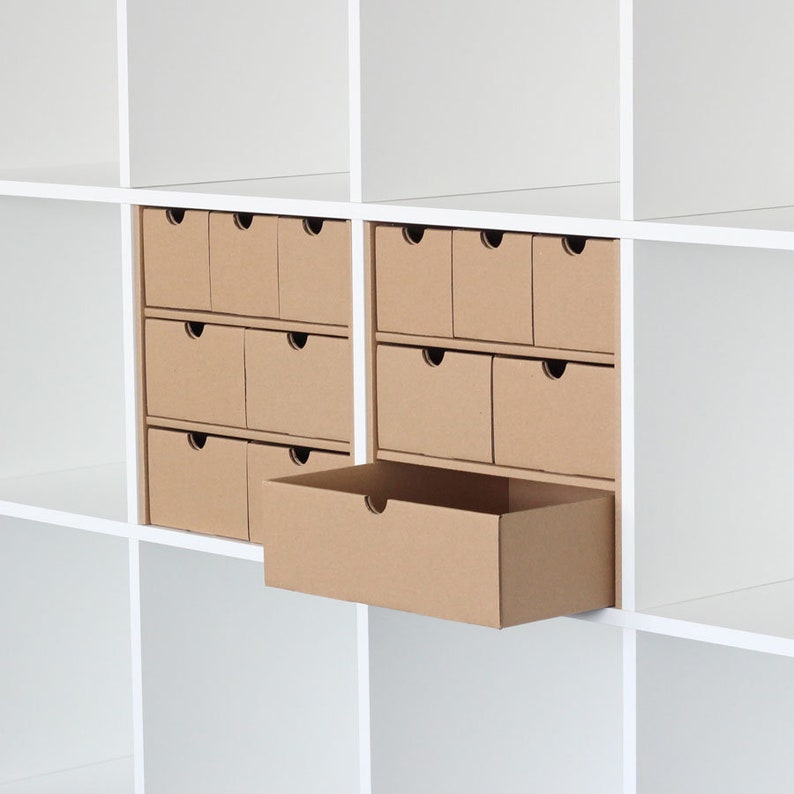 2 Fächer sind in einem weißen Ikea Kallax Regal mit jeweils einem Schubladeneinsatz aus Pappe gefüllt. Ein Einsatz besteht aus 7 Schubladen, der andere aus 6 Schublade.