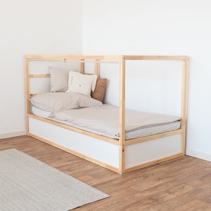 Ikea Kura Kinderbett, das mit Kissen und einer Bettdecke dekoriert wurde. An der Seite wurde am Bett eine Stange für Vorhänge montiert.