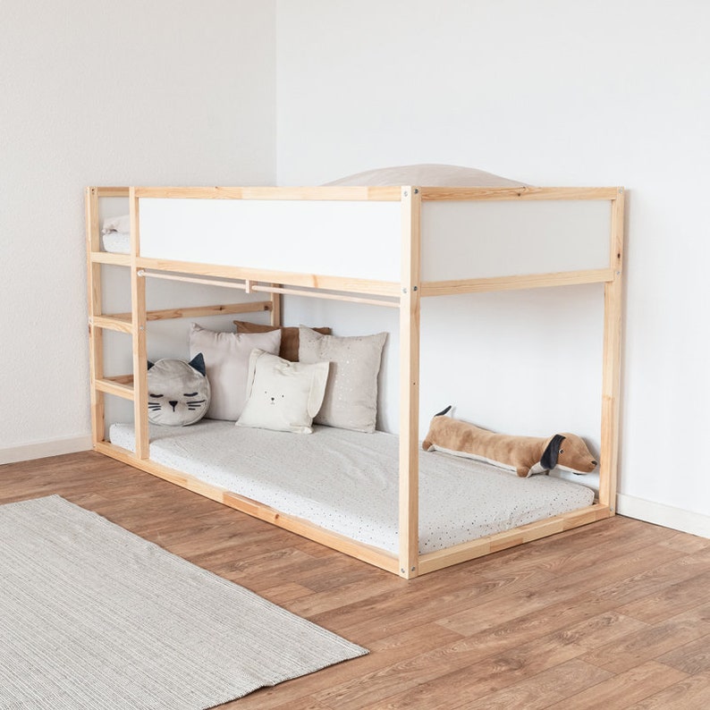 Ikea Kura Kinderbett, das mit Kuscheltieren und anderen Textilien dekoriert wurde. An der Seite wurde am Bett eine Stange für Vorhänge montiert.