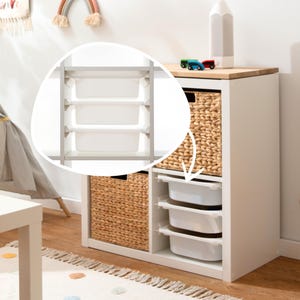 Op de afbeelding: Witte opbergkast met drie uitschuifbare witte bakken en twee geweven manden. De kast heeft een licht houten blad en is versierd met een regenboog en een potloodvormige lamp. Twee speelgoedauto's staan bovenop.