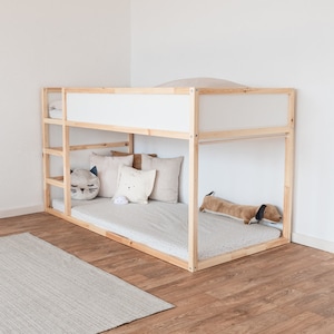 Ikea Kura Kinderbett, das mit Kuscheltieren und anderen Textilien dekoriert wurde. An der Fußseite wurde am Bett eine Stange für Vorhänge montiert.