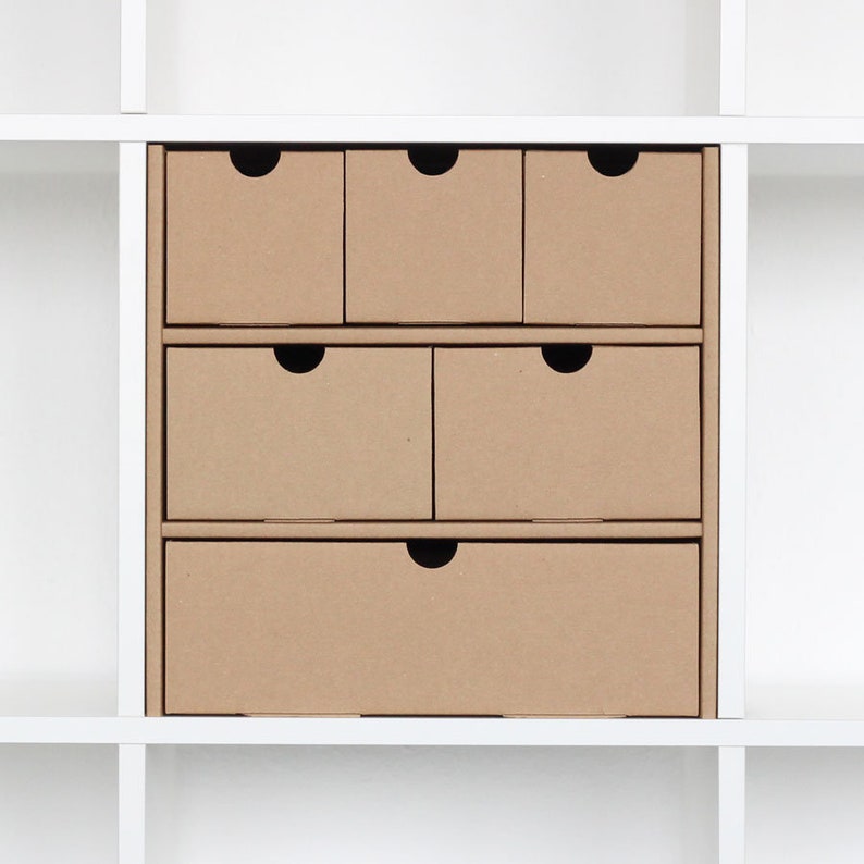 Ein Fach in einem weißen Ikea Kallax Regal ist mit einem Schubladeneinsatz mit 6 Schubladen aus Pappe gefüllt.