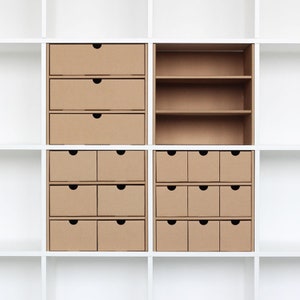 4 Fächer in einem weißen Ikea Kallax Regal sind mit jeweils 4 verschiedenen Schubladeneinsätzen aus Pappe gefüllt. Ein Einsatz ist auf dem Bild ohne Schubladen zu sehen.