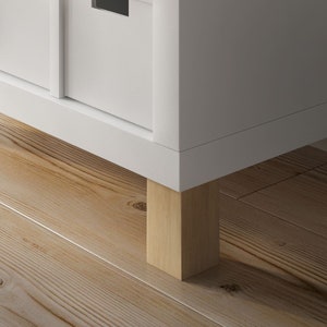 Ein weißes Ikea Kallax Regal steht auf quadratischen Möbelfüßen aus Buchenholz.