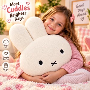 May include: A white plush rabbit-shaped pillow with black embroidered eyes and an X-shaped mouth. The text on the image reads: More Cuddles Brighter Days, Super Soft, Huggable Comfort, Perfect Gift, and Good Days Ahead with heart icons.