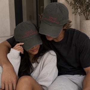 Puede incluir: Dos gorras de béisbol gris carbón con el texto rojo bordado "ceo of overthinking" en la parte delantera. Cada gorra tiene una corona estructurada, una visera curva y un acabado desgastado a lo largo de los bordes de la visera.