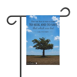 Könnte beinhalten: Eine rechteckige Gartenflagge, die an einem schwarzen Metallständer hängt. Die Flagge zeigt einen blauen Himmel mit weißen Wolken über einem braunen Feld und einem einzelnen Baum. Der Text lautet: FOR THE SON OF MAN IS COME TO SEEK AND TO SAVE that which was lost. Luke 19:10 (KJV).