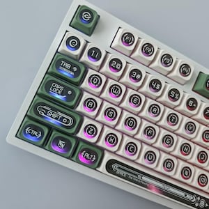 May include: A mechanical keyboard featuring a white frame and a mix of white and olive green keycaps. The keys display circular icons and letters with purple and blue backlighting. The space bar includes the text SPACE - The Time is Flowing.