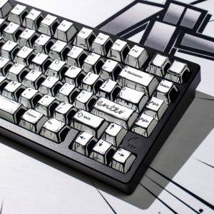 May include: A black mechanical keyboard featuring white keycaps with black ink-style comic book outlines and shading. The keycaps display standard alphanumeric characters, function keys, and a stylized enter key with the word enter written in script.