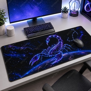 May include: A rectangular desk mat featuring a vibrant, glowing purple and blue scorpion graphic set against a dark space background with stars and a planet. The design includes a constellation pattern in the upper right corner of the mat.