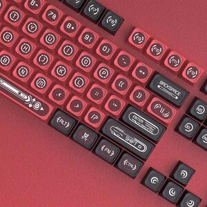 May include: A mechanical keyboard with a red and black color scheme. The keys feature custom circular icons and symbols. Specific keys are labeled with text including BACKSPACE, ENTER, SPACE OF TIME, and SHIFT, set against a textured red base.
