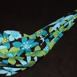 Puede incluir: Una bolsa de tela con un patrón floral en tonos azules, verdes y marrones. La bolsa está doblada y colocada sobre una superficie oscura.