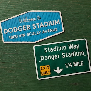 May include: Two rectangular signs. The top sign is blue with white text reading Welcome to DODGER STADIUM 1000 VIN SCULLY AVENUE. The bottom sign is green with white text reading Stadium Way Dodger Stadium 1/4 MILE and a yellow EXIT ONLY box.