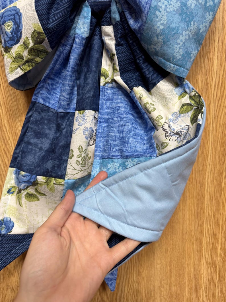 Pu&ograve; includere: Un pezzo di tessuto trapuntato con un design patchwork di vari motivi blu e bianchi, inclusi disegni floreali, farfalle e texture a spina di pesce. Il retro &egrave; in tessuto azzurro tinta unita con cuciture visibili.