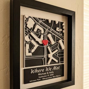 May include: A framed 3D map art piece featuring a black and white street layout with a red heart marker. Below the map, a black plaque displays the text: Where We Met, Michael & Holly, September 19, 2004, Johnson Park - Albuquerque, New Mexico.