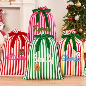 Pode incluir: Quatro sacos de presente de Natal em tecido com riscas verticais vermelhas, brancas e verdes. Cada saco é atado no topo com uma fita de veludo e apresenta um nome personalizado em relevo, incluindo Karen, Alison, Emily e Gloria.