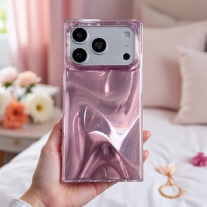 May include: A rectangular smartphone case featuring a metallic, liquid-like rose gold finish with a wavy, reflective surface. The upper section includes a silver-toned camera module housing three circular lenses and a small circular flash aperture.