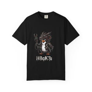 May include: A black short-sleeve t-shirt featuring a graphic of a penguin wearing a dragon-like headpiece and a dark jacket, holding a staff. Below the character, the text H8CK3r is printed in a distressed, white, stencil-style font.