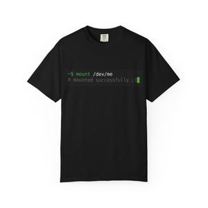 Puede incluir: Una camiseta negra de manga corta con un estampado gráfico de una línea de comandos de terminal de ordenador. El texto dice: ~$ mount /dev/me # mounted successfully ;) con la palabra mount y el bloque del cursor en verde sobre fondo oscuro.