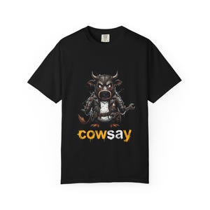 Puede incluir: Una camiseta negra de manga corta con un gráfico de un toro de dibujos animados que lleva una chaqueta de cuero y sostiene una llave inglesa. Debajo del toro, la palabra "cowsay" está impresa en una fuente amarilla desgastada con salpicaduras.