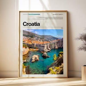 May include: A vertical wall art print featuring a photograph of the coastal city of Dubrovnik, Croatia, with its iconic stone walls, orange rooftops, and turquoise water. The text Croatia is printed in bold black letters above the image.