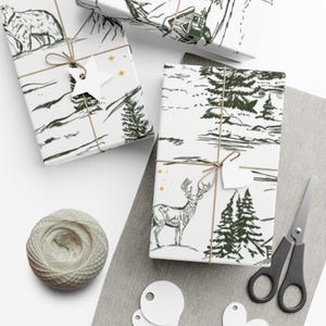 May include: White wrapping paper featuring a dark green ink illustration of a deer, pine trees, and snowy landscapes, tied with brown twine and a white heart-shaped gift tag, accompanied by a ball of twine, scissors, and blank gift tags.