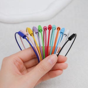 May include: A collection of twelve thin, flexible wire cable key rings in a variety of vibrant colors including blue, pink, yellow, purple, green, red, turquoise, orange, white, and black, each featuring a secure, threaded screw-lock barrel.