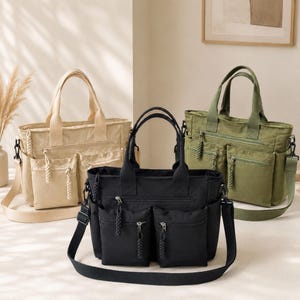 May include: Three canvas tote bags in beige, black, and olive green. Each bag features two top handles, a detachable shoulder strap, a main zippered compartment, and two front exterior pockets with braided zipper pulls for easy access.
