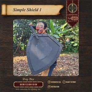 Op de afbeelding: Een donkergrijs schild-rekwisiet met een puntige onderkant en een centraal schildvormig embleem, voorzien van een rand met cirkelvormige klinknageldetails. De tekst Simple Shield 1, A4 PDF en de afmetingen 60 cm x 3,5 cm x 53 cm zijn zichtbaar.