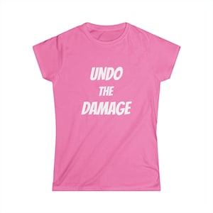 May include: A bright pink short-sleeved t-shirt featuring the text "UNDO THE DAMAGE" printed in bold white capital letters across the center of the chest. The garment has a classic crew neckline and a straight hemline, providing a simple design.